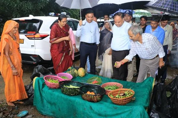 बारिश के बीच खेत की उपज से भरी टोकरियों और मेज के पास खड़े अधिकारी तथा ग्रामीण